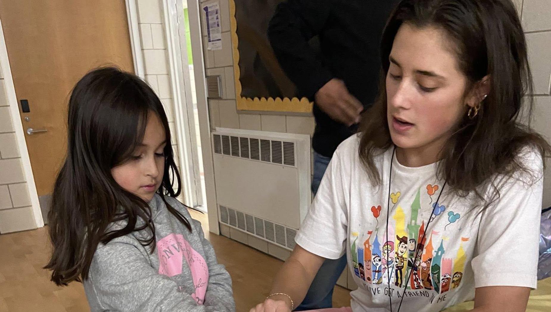A child watches an adult apply a temporary tattoo with various characters on the table.