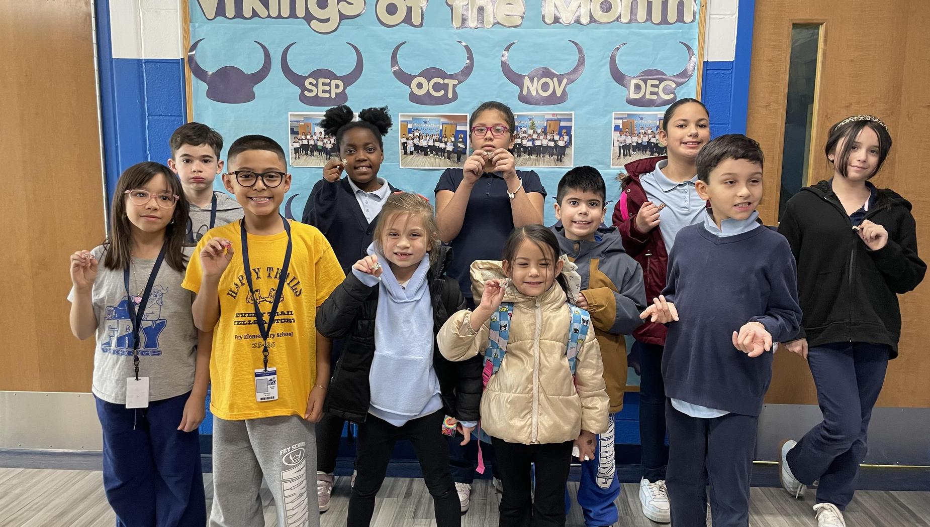 Group of children posing in front of a school display board.