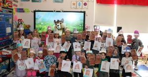 class of kindergartners holding up puppets, drawings and wearing groundhog crowns