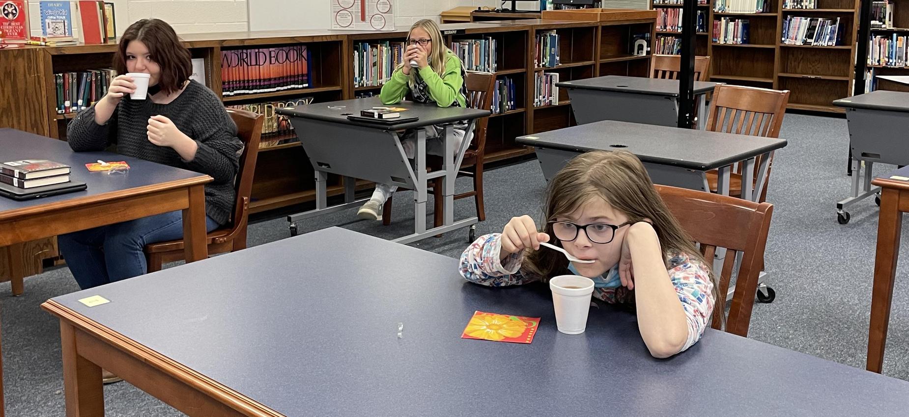 Three students drink tea in a library.