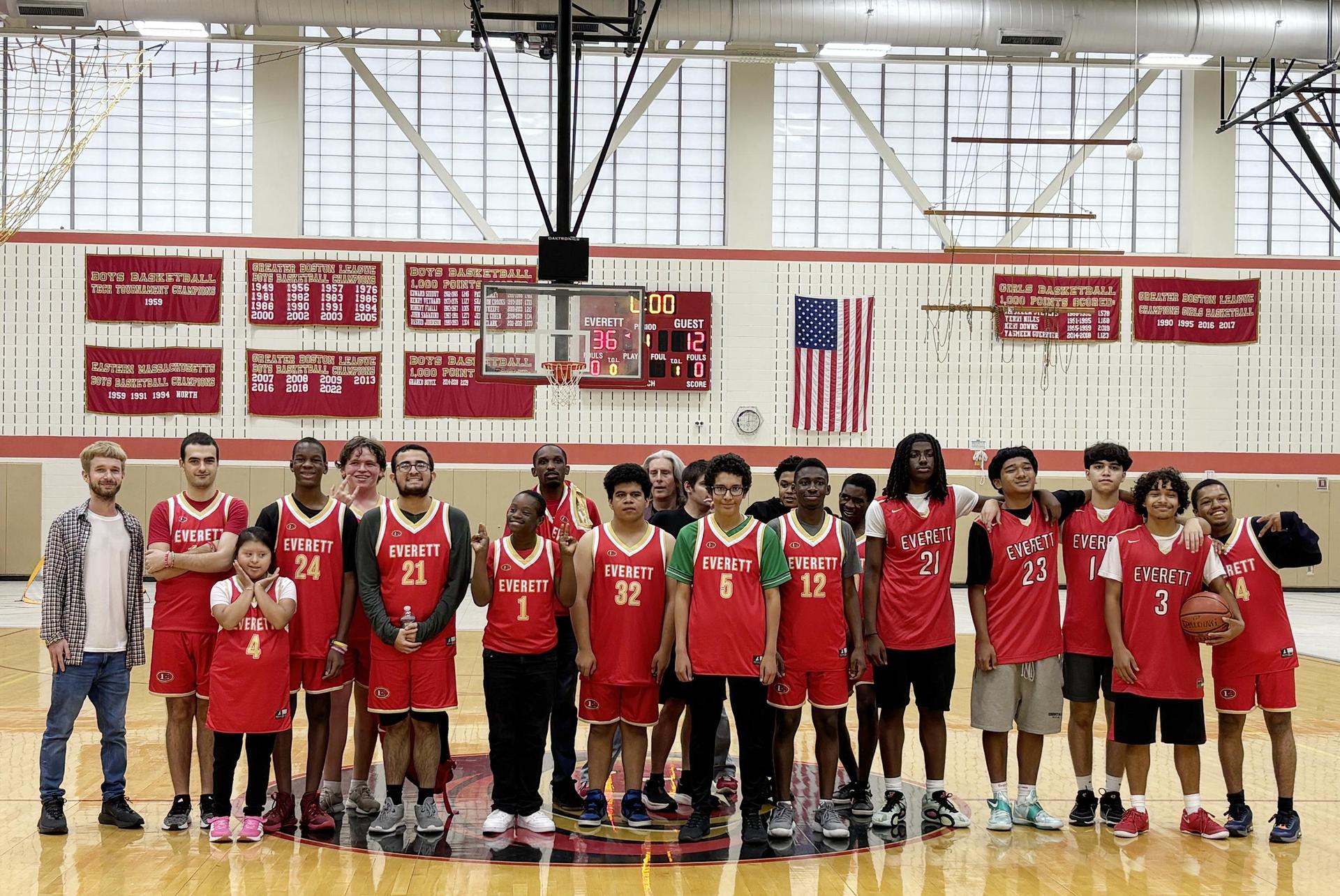 Basketball team and supporters in red jerseys posing in a gymnasium.
