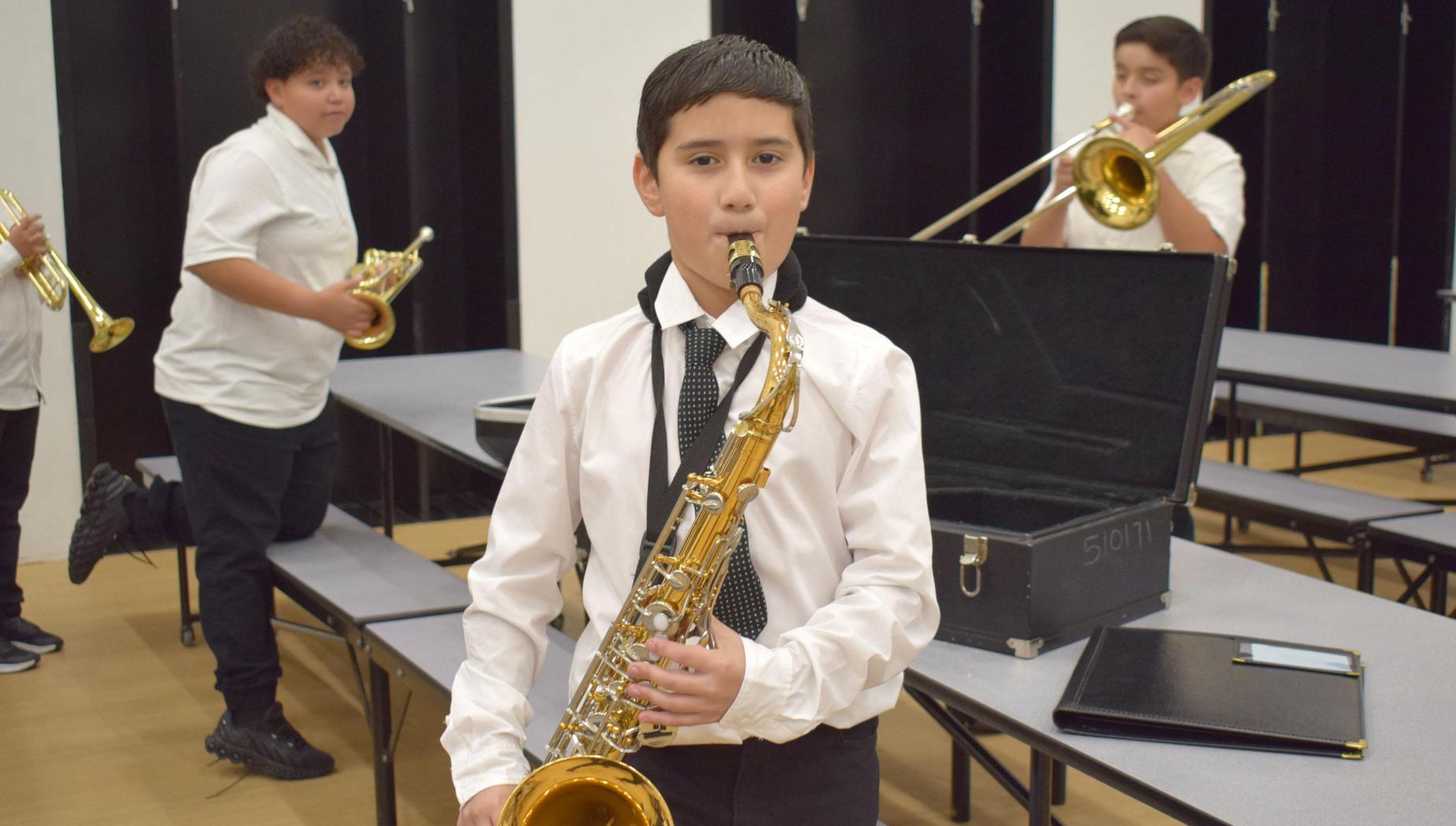 A boy plays a saxophone with other musicians in the background holding instruments.