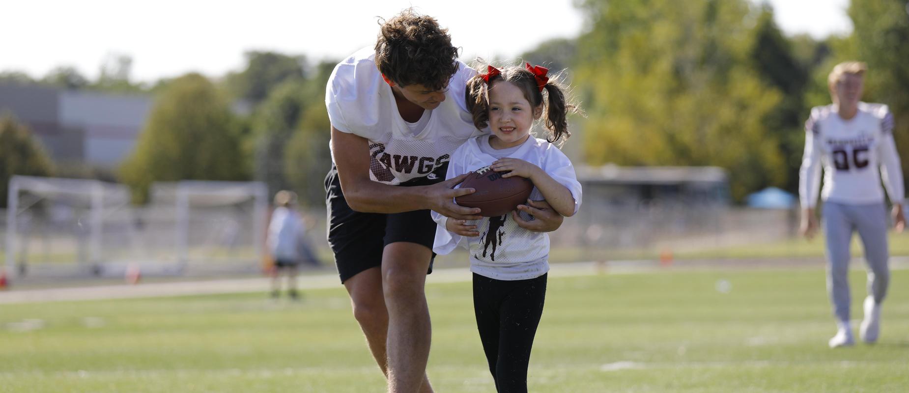 football player helps young girl cross into the endzone with football