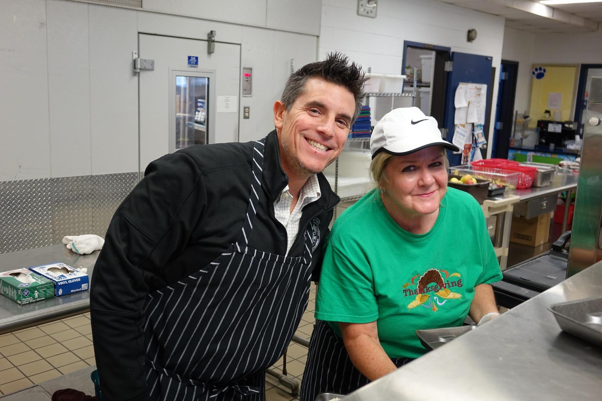 A man and a woman in aprons smiling in a kitchen.