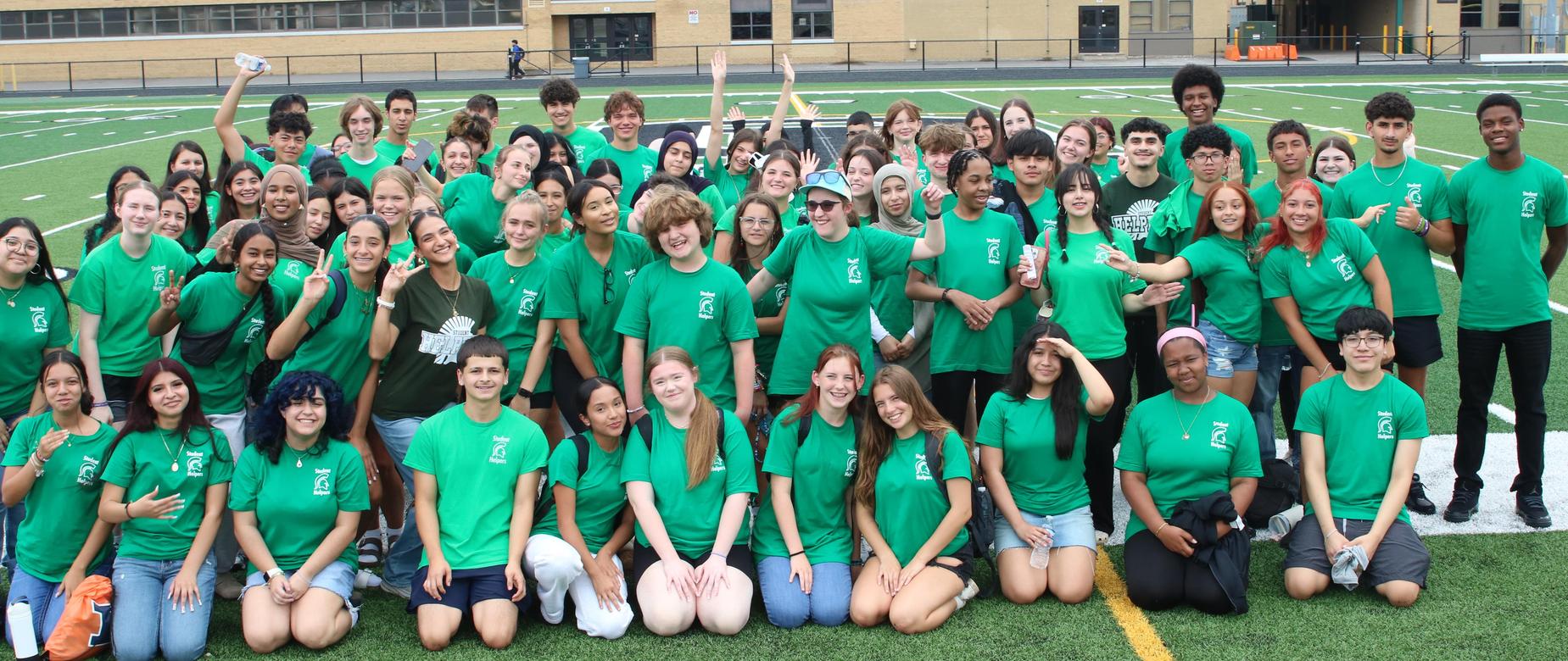 Picture of students in green shirts on football field.
