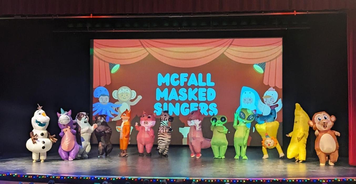 Performers in colorful costumes on stage, with a backdrop reading 'McFall Masked Singers'.
