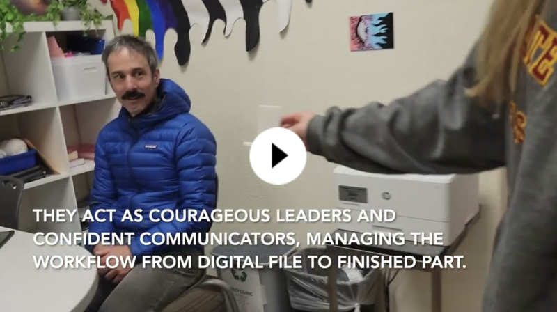 Adult sitting in a classroom looks toward someone standing near a printer, with text overlaid on the video frame.