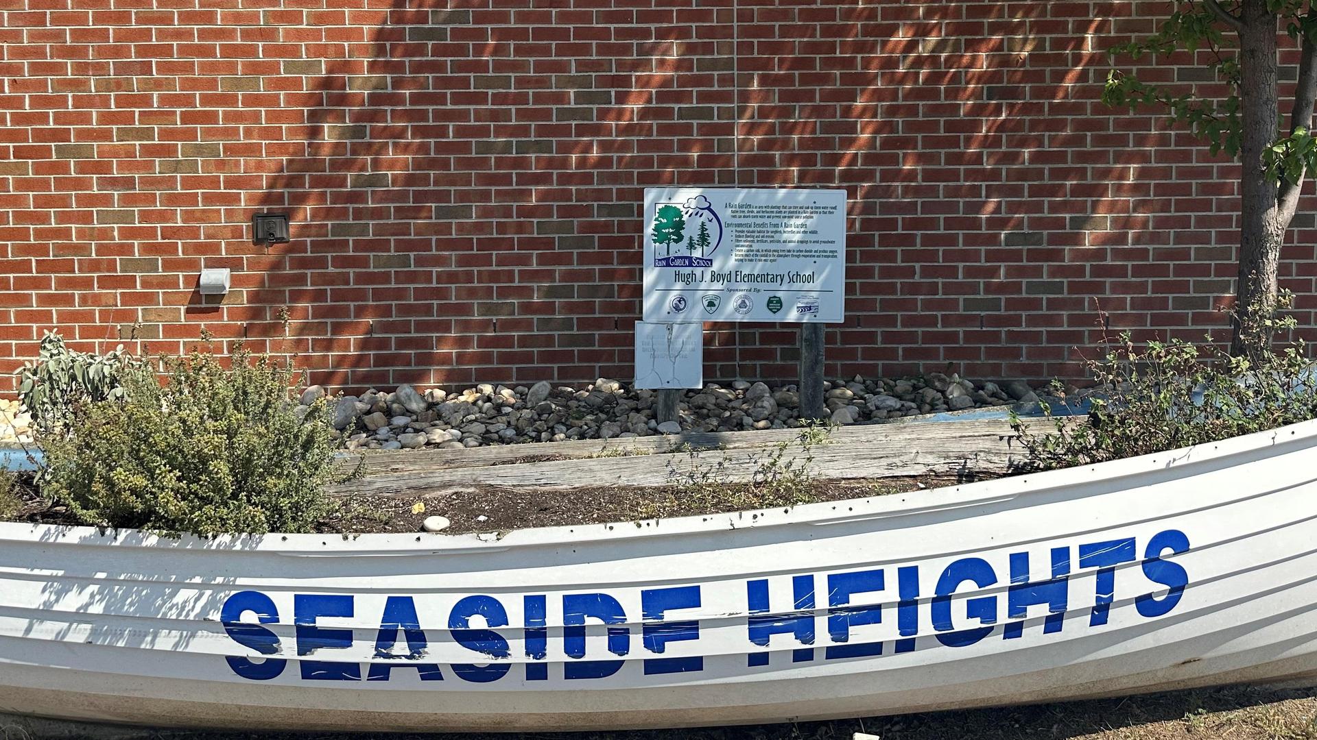 A boat planter with the words 'SEASIDE HEIGHTS' and a sign in front of a brick wall.