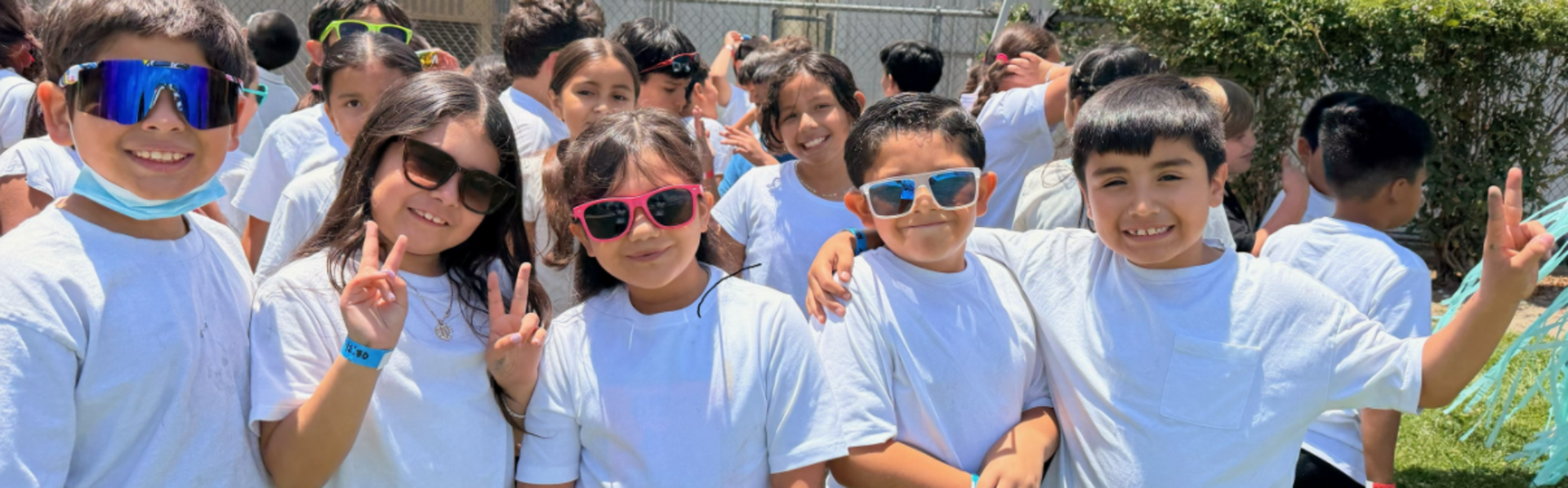 Group of children with sunglasses, wearing white t-shirts, smiling together outdoors.