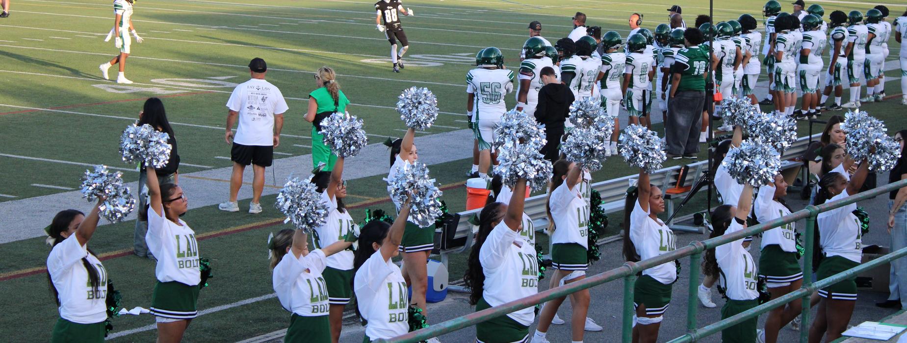 CHSE cheerleaders performing with CHSE football players lined up watching the injury fund game on the field.