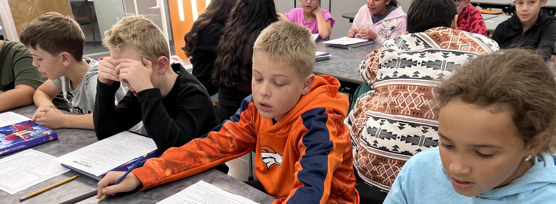 Two students focused on their work at a table with books and papers laid out.