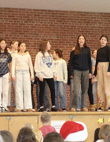 A group of children performing on stage in front of a brick wall.