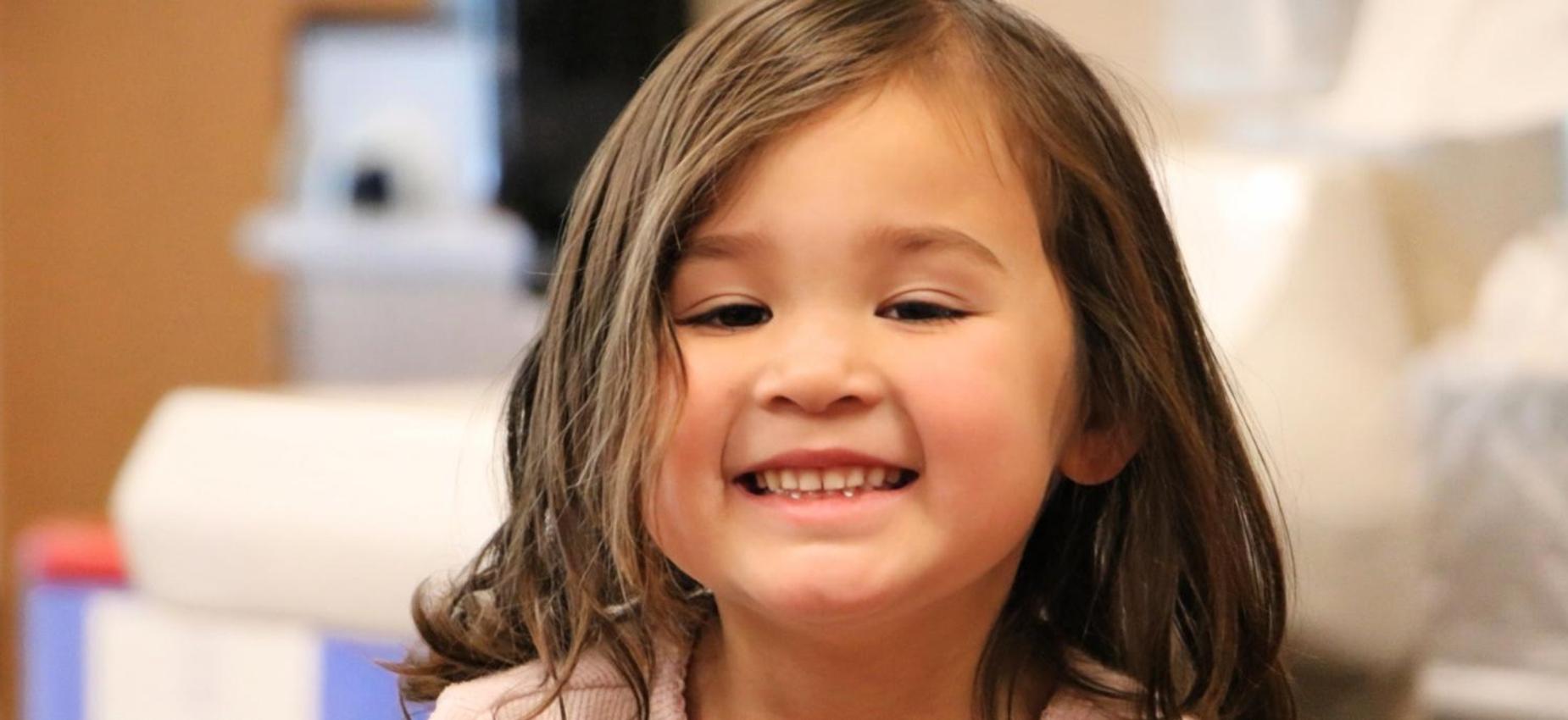 Smiling girl in a classroom with light brown hair.