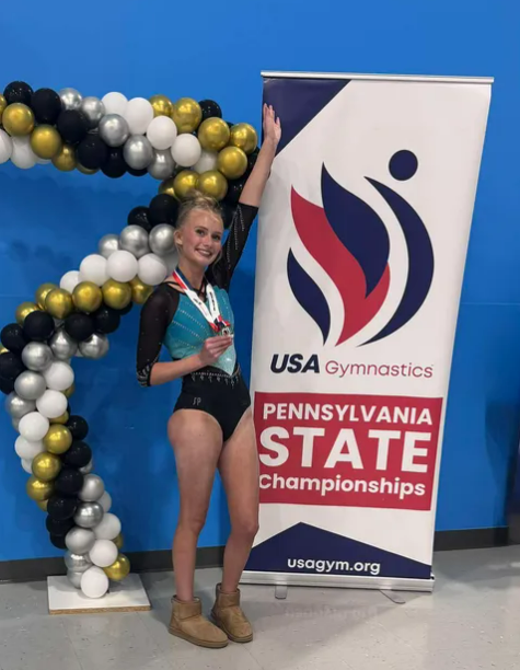 girl in gymnastic leotard holding medal in front of states sign