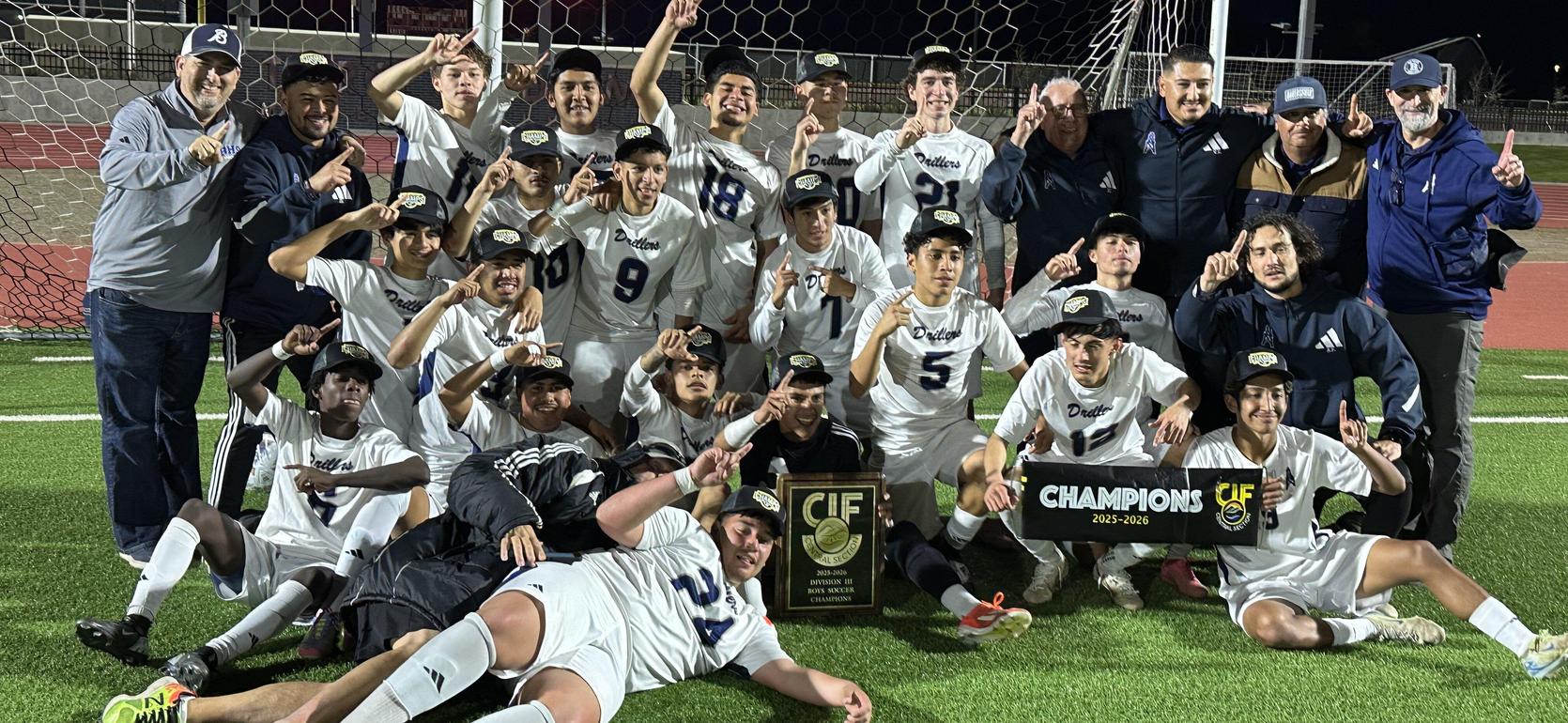 A victorious soccer team celebrates with trophies and a banner on a field.