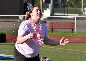 Girl in a floral lei laughs while droplets of water splash around her on a field.