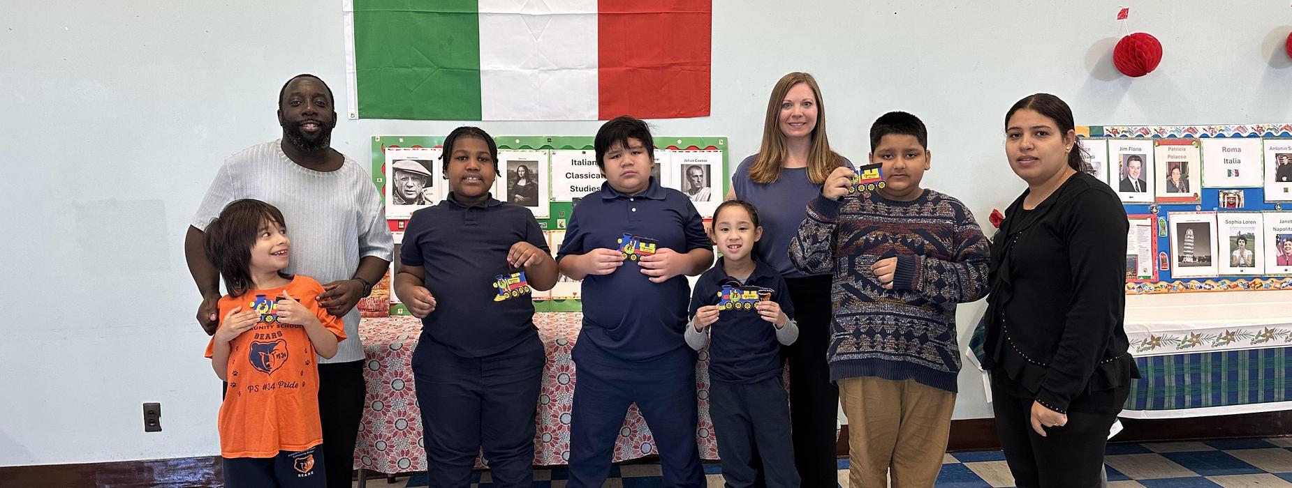 Group of children and adults posing with awards in front of an Italian flag.