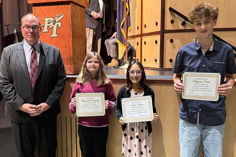 A man and three students holding certificates stand in front of a stage