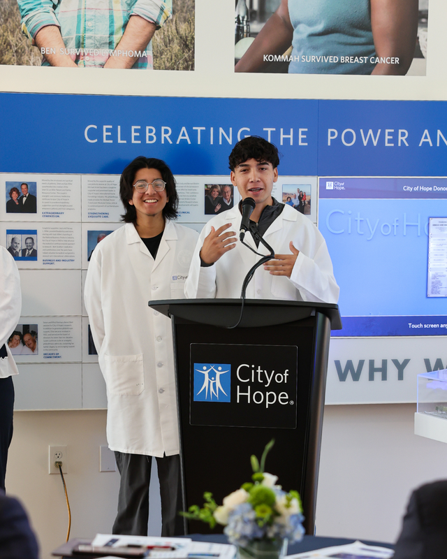 Two student interns in lab coats presenting at City of Hope