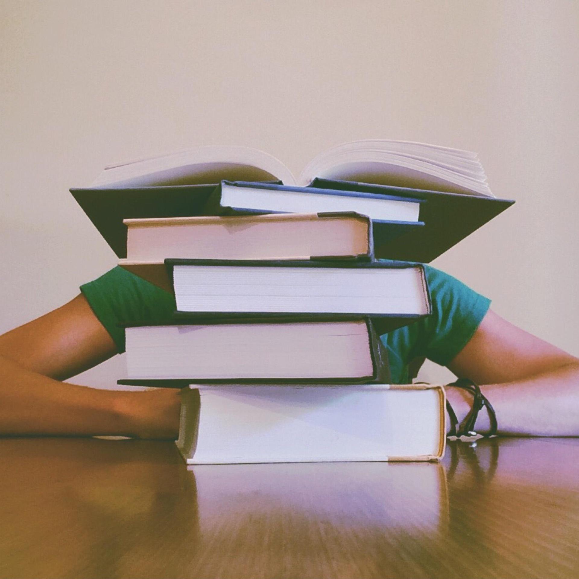 A person resting their arms on a stack of books with an open book on top.