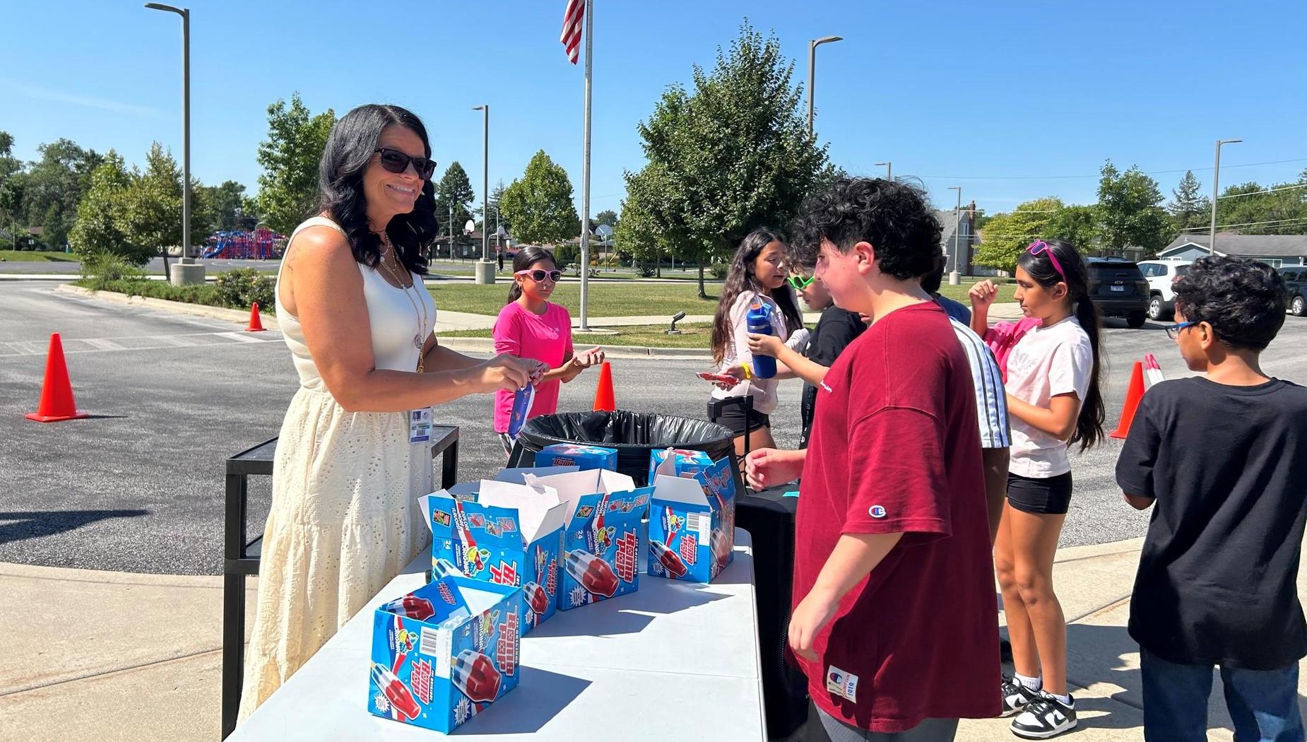Woman serving ice pops to kids at a sunny outdoor event.