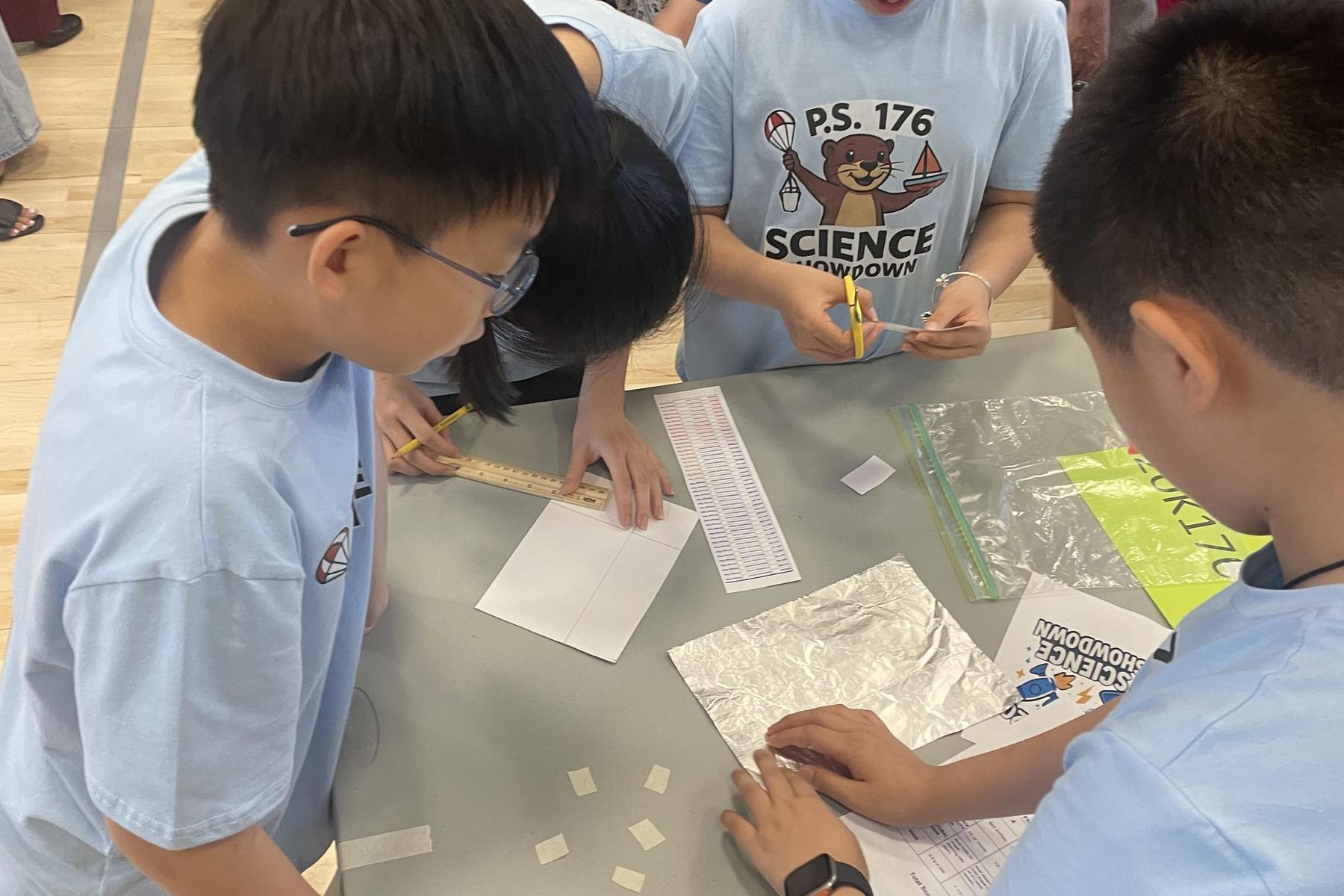 Group of children working together with tools, paper, and scissors at a table.