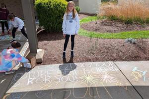 A student stands on the sidewalk next to the artwork she created from chalk