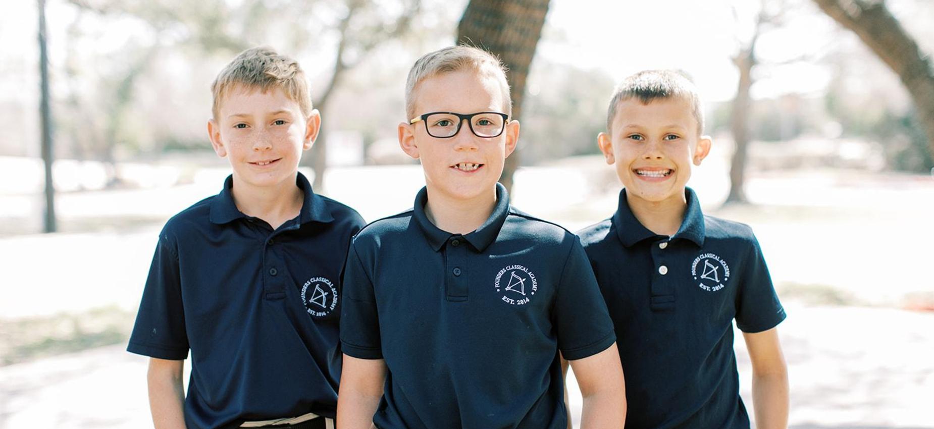 Three smiling elementary boys in Founders polos outside