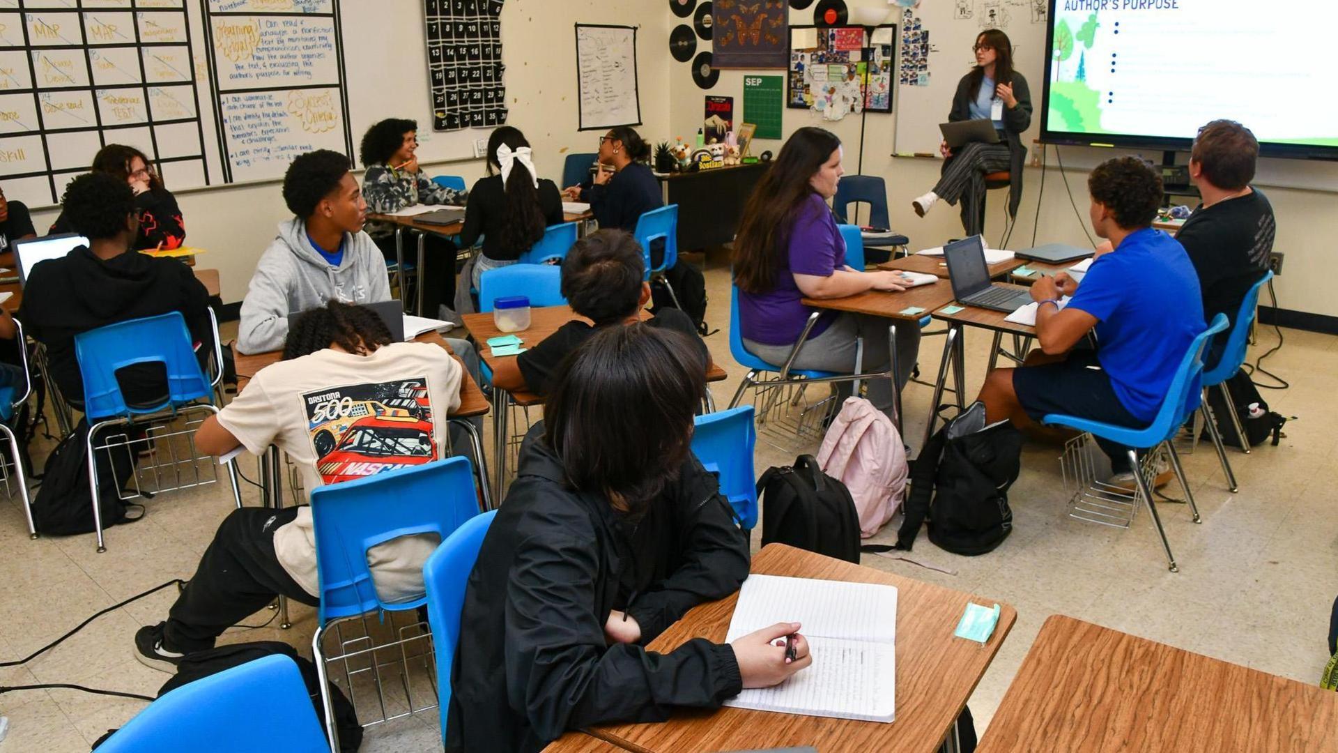 Students engaged in a classroom with a teacher presenting at the front.