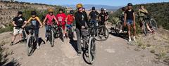 A group of teenagers on bikes posing atop a rock formation with mountains in the background.