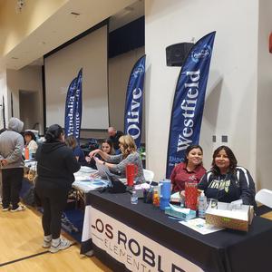 School representatives from multiple PUSD elementary schools greet families at registration tables during the Kinder Round-Up event.