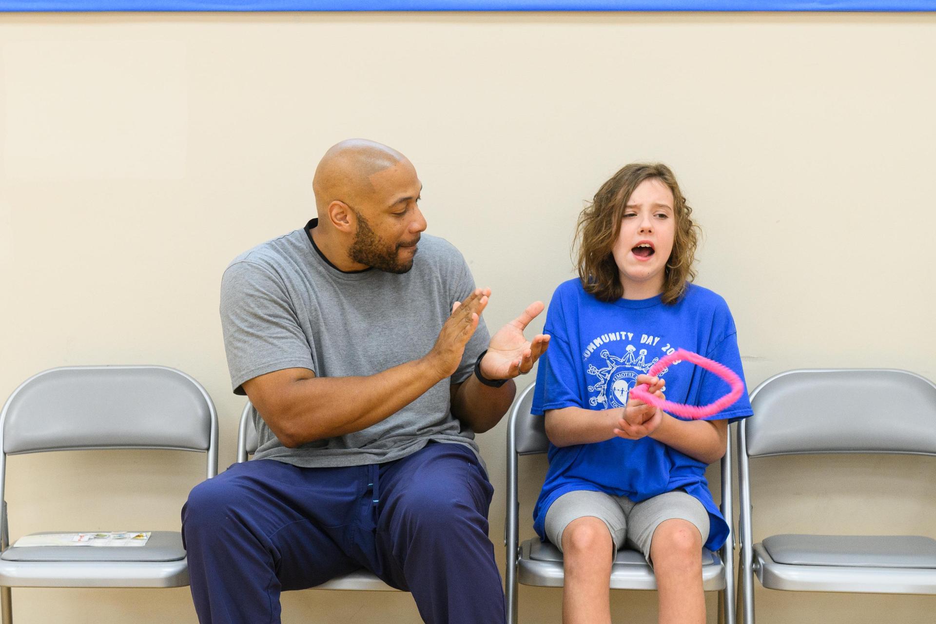 Teacher and student sitting on a bench in the gym clapping.
