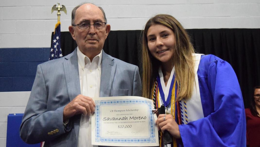 A graduate holding a scholarship certificate next to an older man.