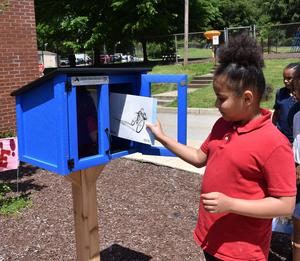 student in red shirt placing book in blue library box