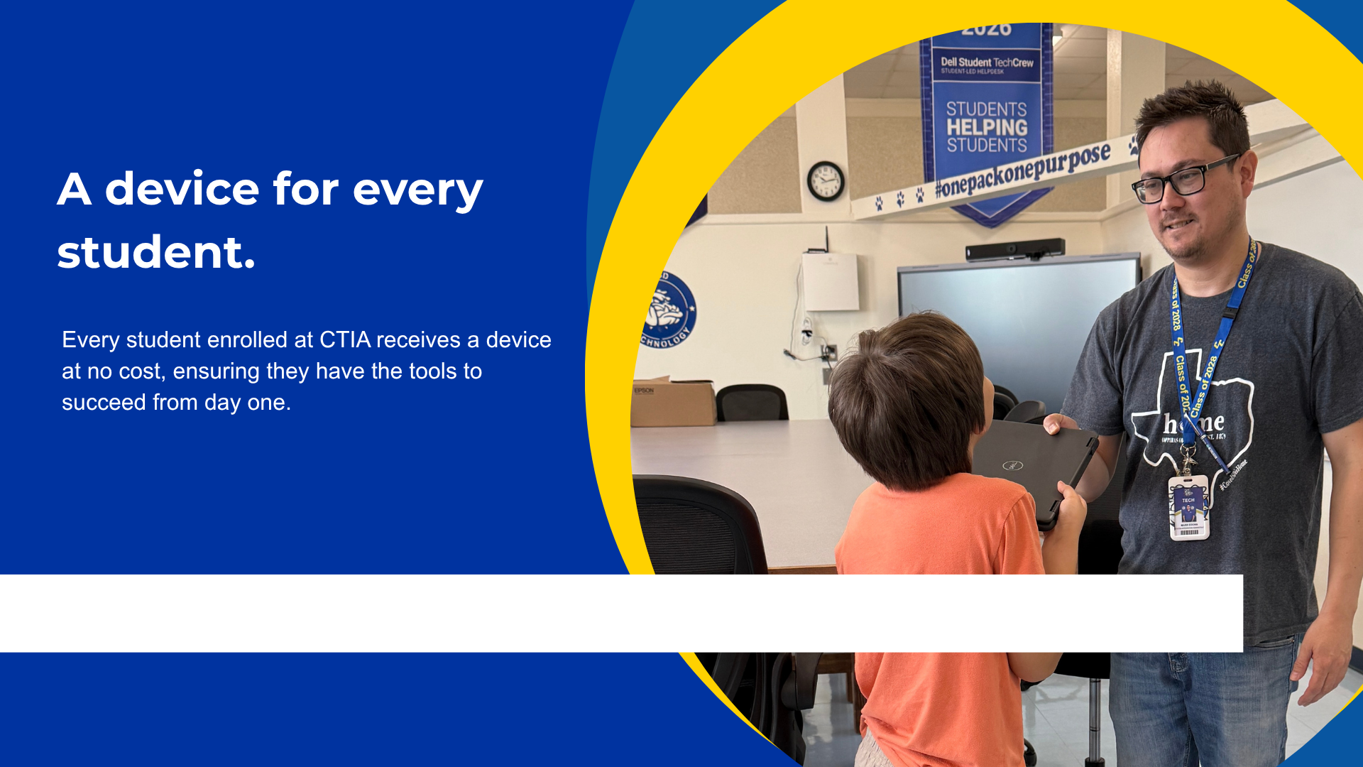 A teacher handing a laptop to a young student in a classroom setting.