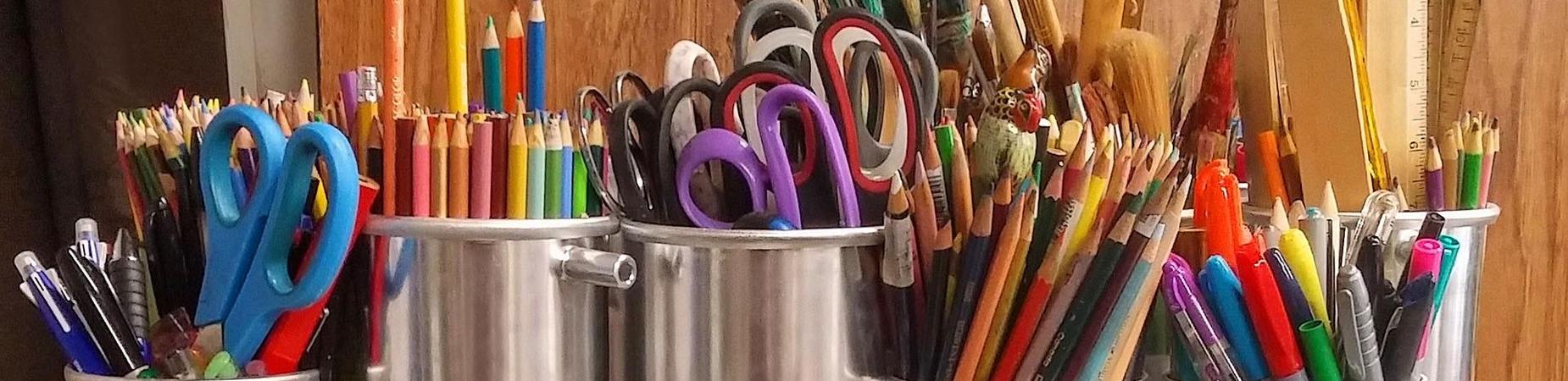 Colorful art supplies including scissors, pencils, and pens in containers.