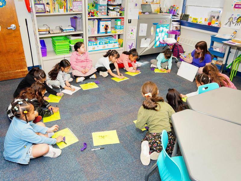 Young students sitting in a circle in class with their teacher.