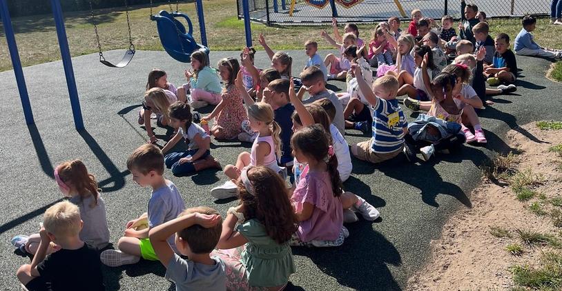 Children in casual attire sit on a playground waiting for their turn to swing.