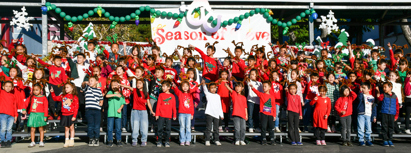Large group of children in holiday attire perform with reindeer antlers at a festive event.