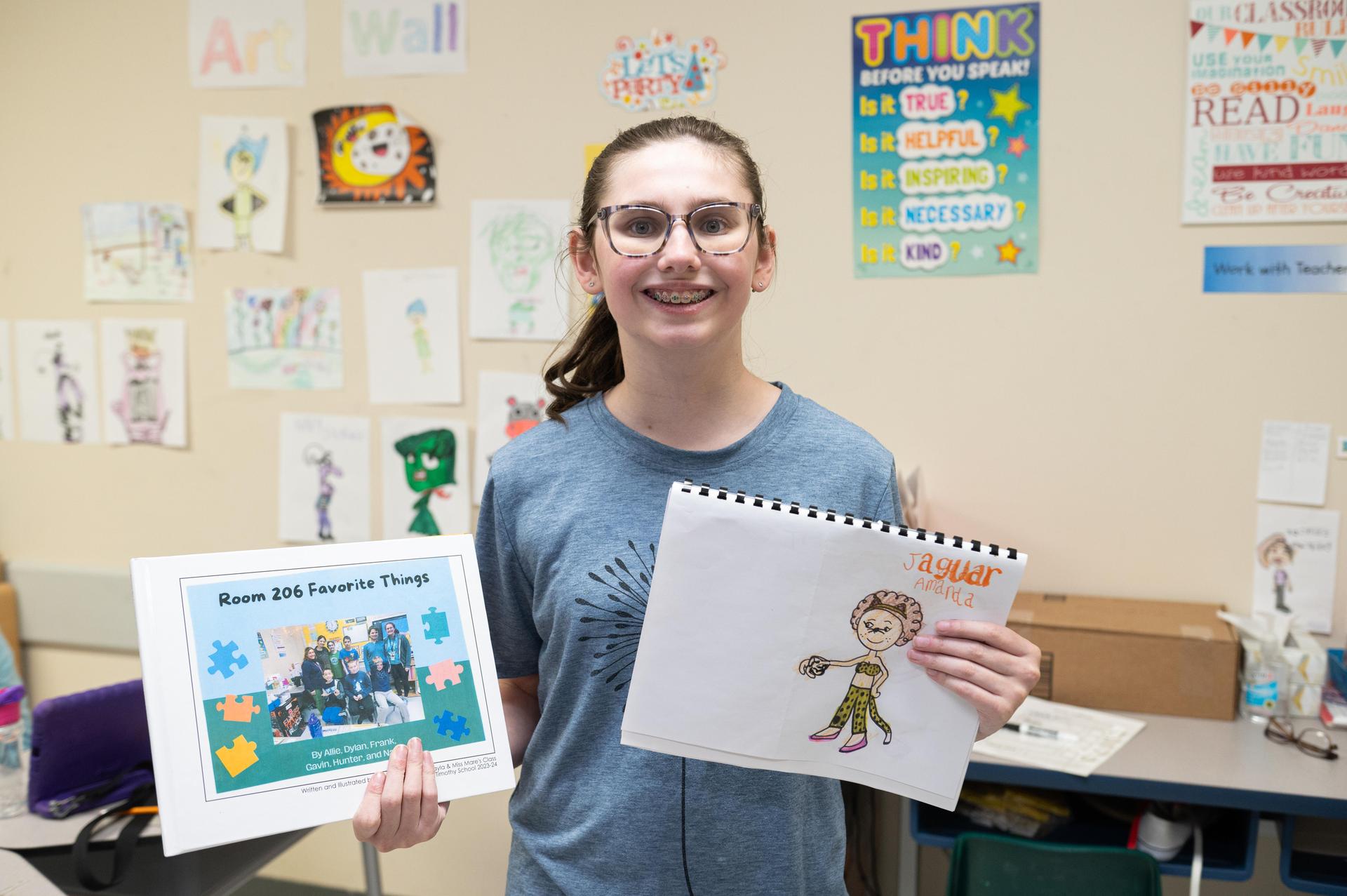 Student holding up a book they wrote and drew.