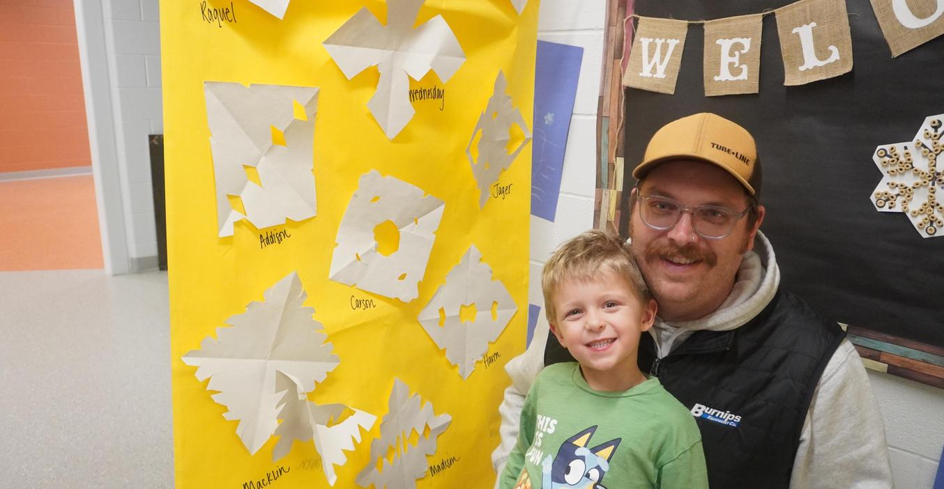 A student and parent pose beside some student artwork made in class.