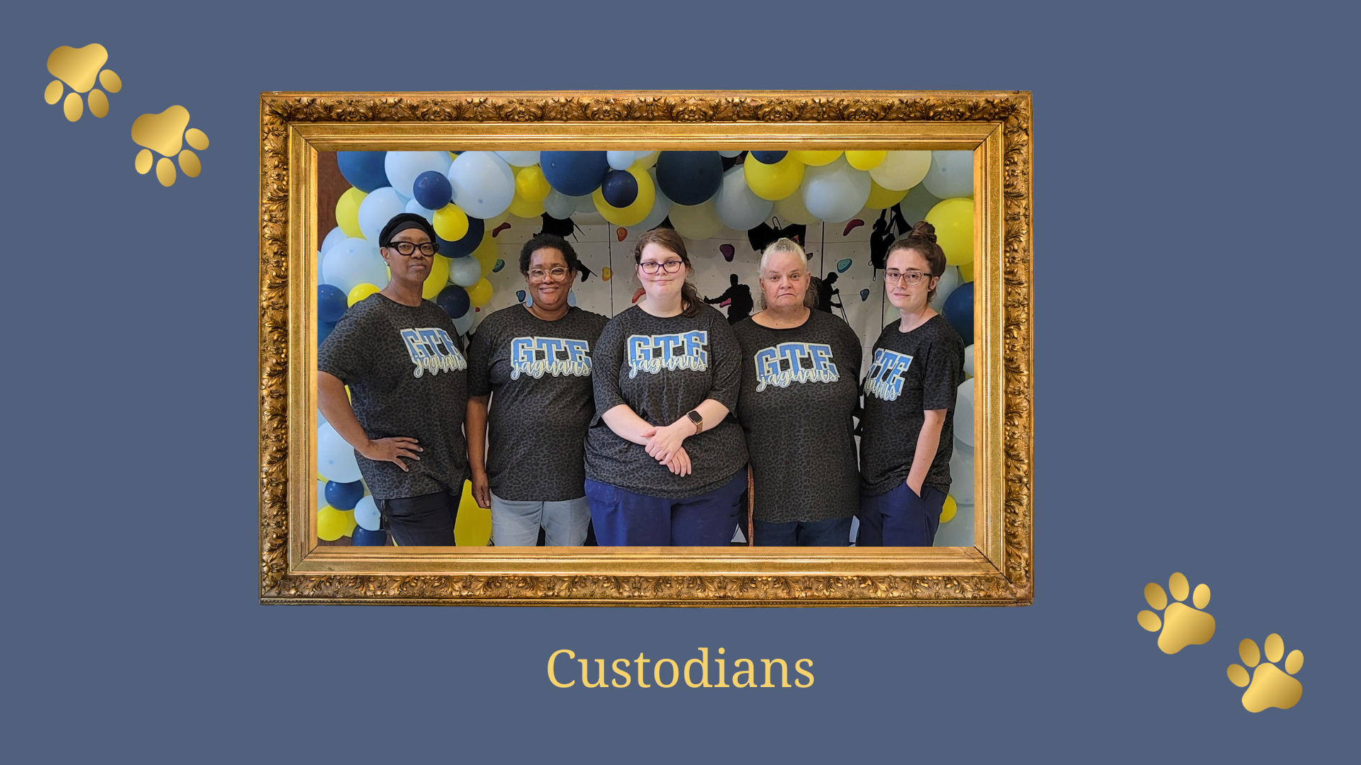 Group of five custodians posing in front of a blue and yellow balloon backdrop.