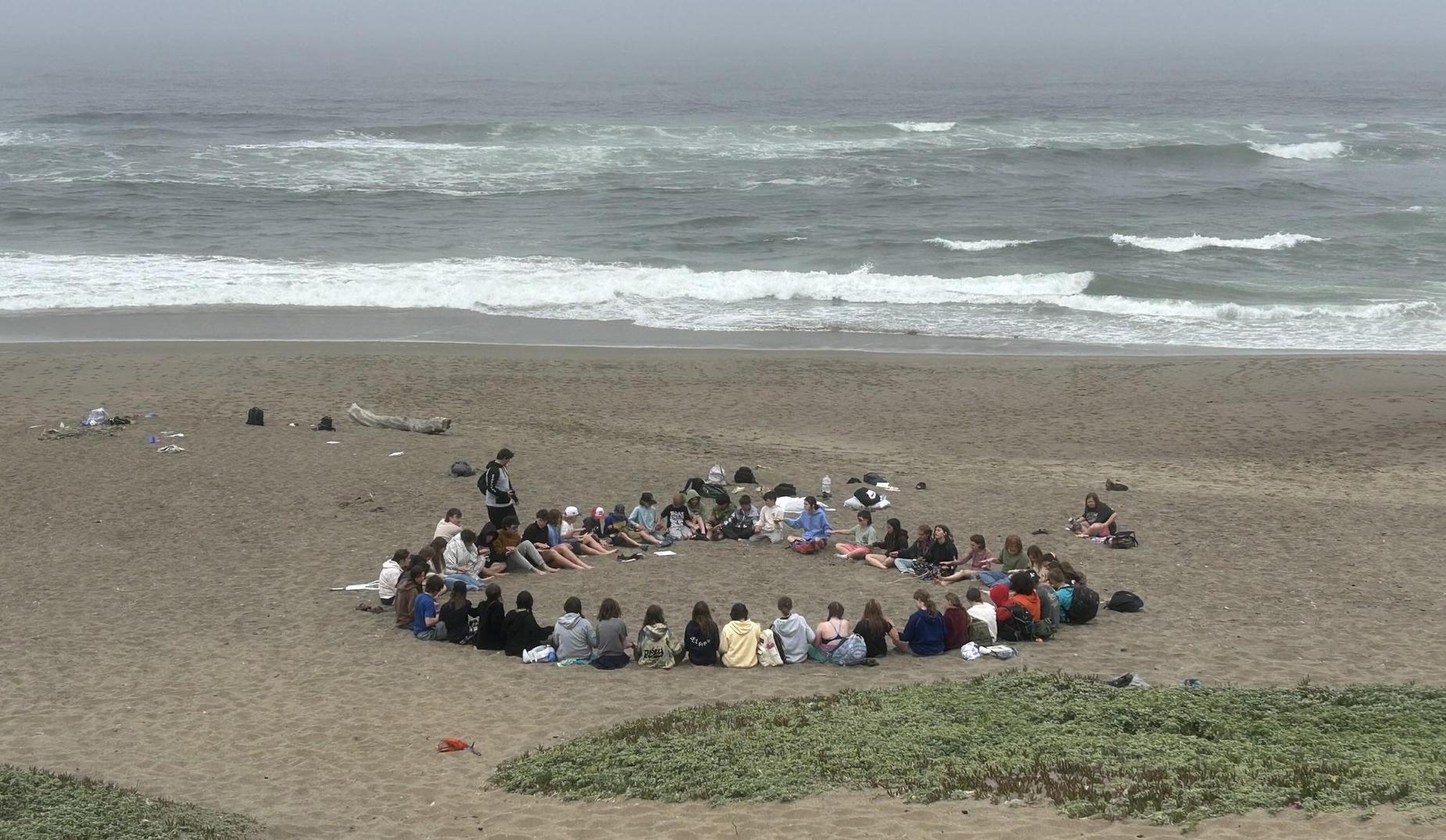Students sit in a circle on the beach in San Francisco