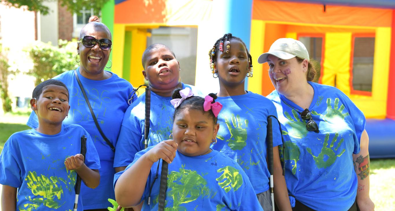 Group of children and adults in blue shirts, smiling outdoors near a bounce house.