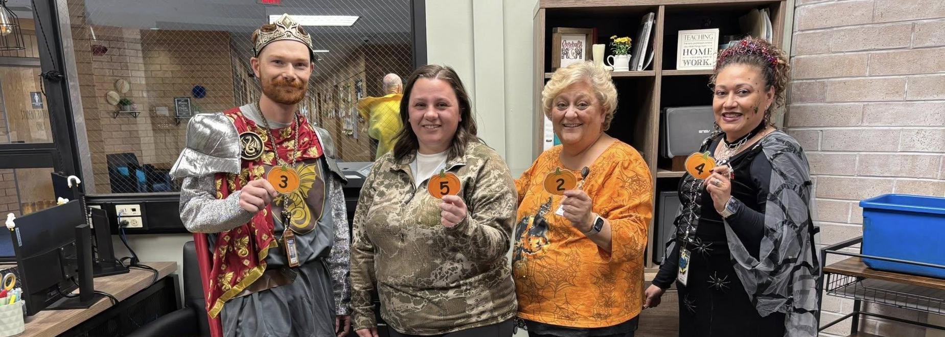 Four individuals in costumes holding numbered signs in a classroom setting.
