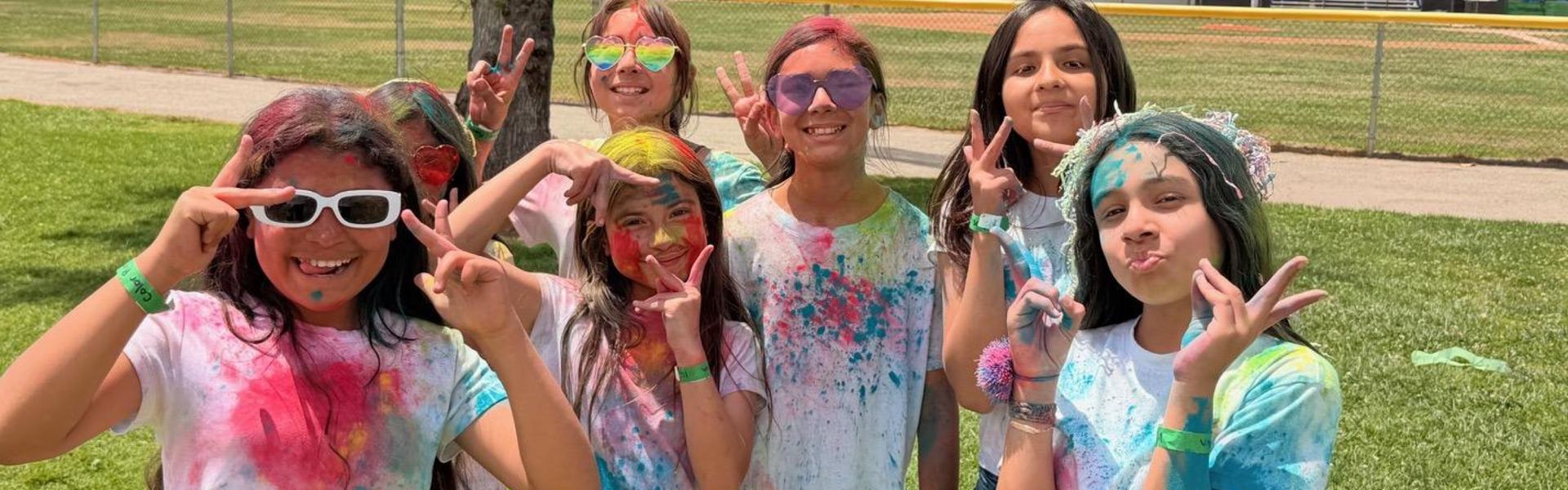 A group of girls smiling and posing with colorful powder on their clothes.