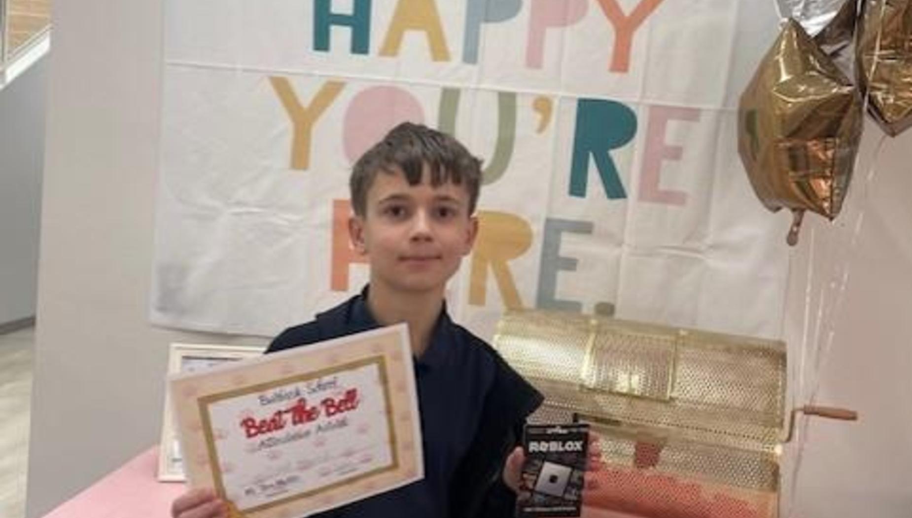 Boy holding a certificate and a box in front of a festive backdrop.