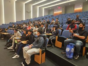 Audience of students seated in a lecture hall with a speaker at the front.