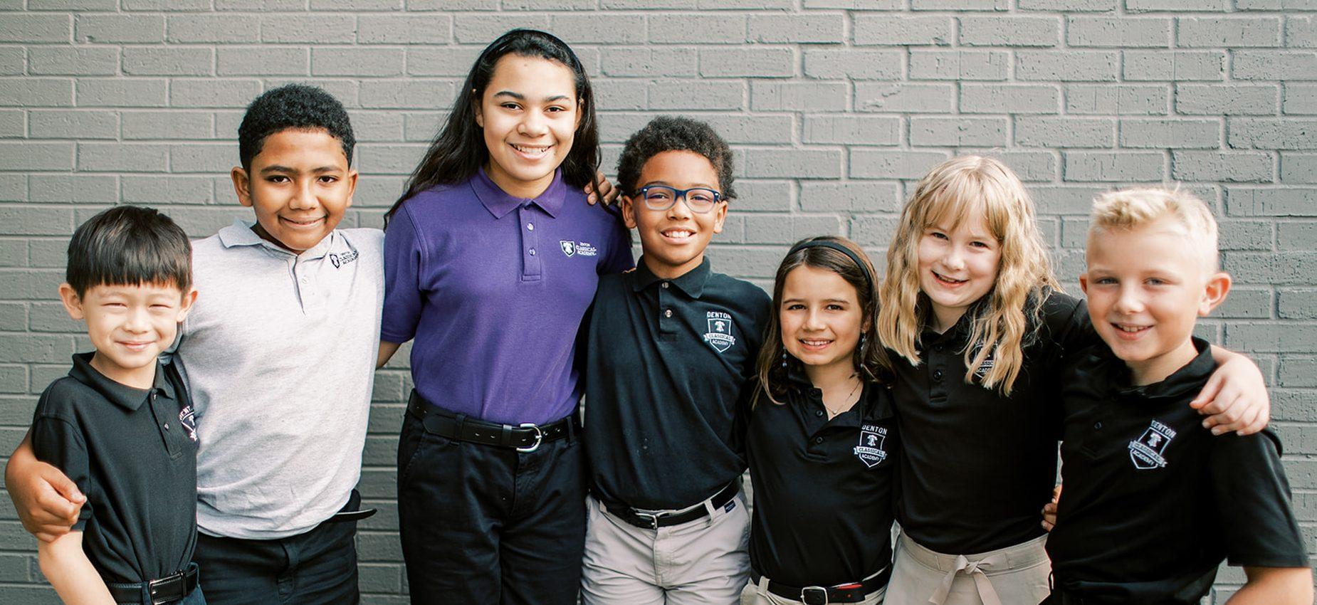 Smiling students in uniform stand together by a brick wall