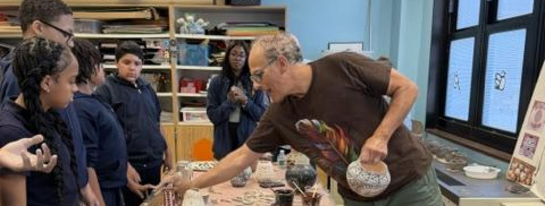 An instructor shows pottery to students while they gather around a table of artifacts.